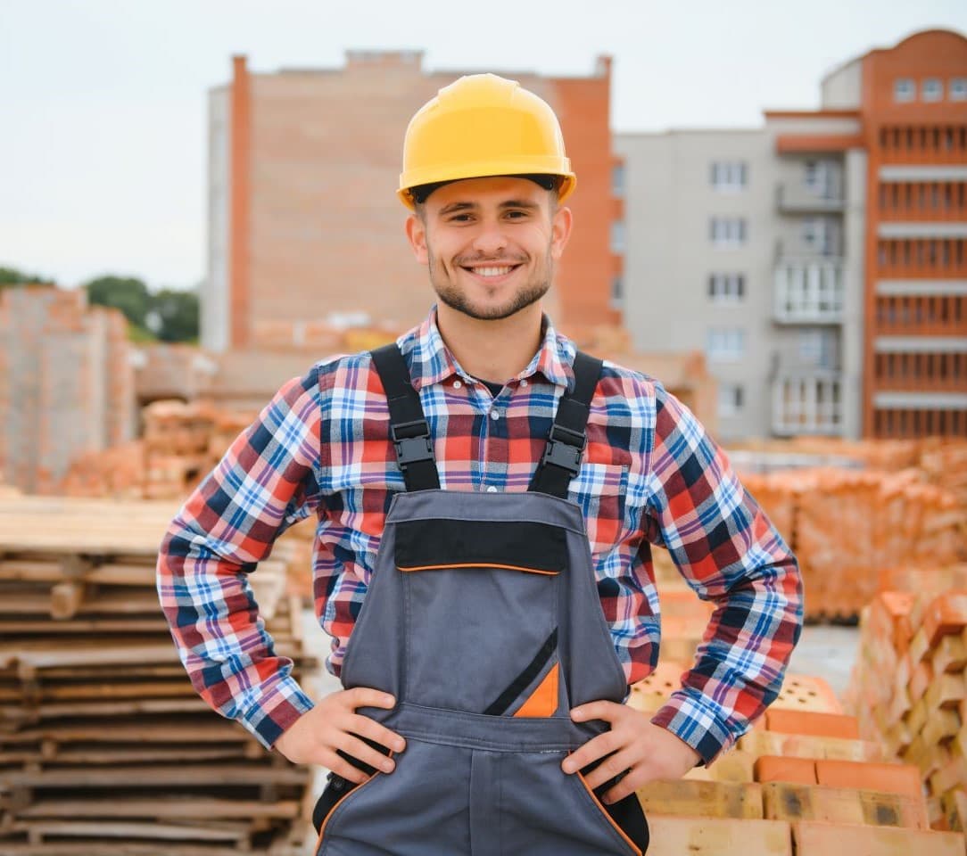 Smiling construction worker bricklayer installing red brick with trowel putty knife outdoors.