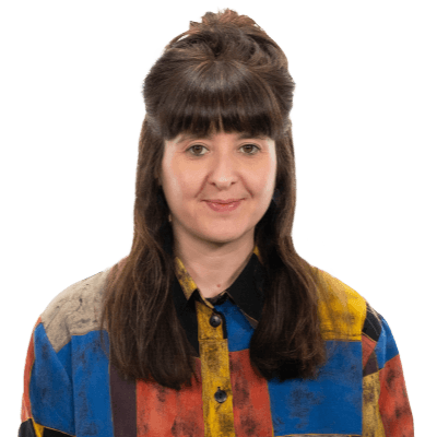 Smiling brunette female with big hair and a colourful shirt.